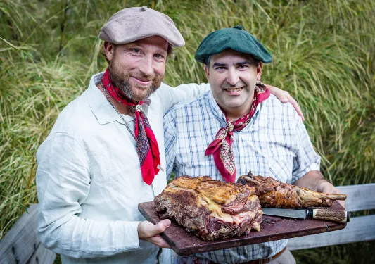 Two locals with meat platter, smiling at camera.