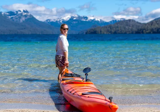 Guest pulling their kayak out to sea, large mountain range behind her.