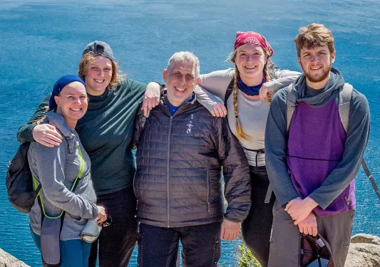 Five guests on cliffside, overlooking large lake, mountains.