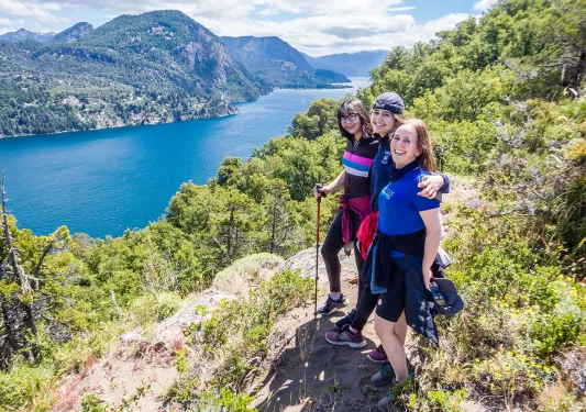 Three young guests posing together, overlooking large lake, hillside.