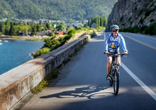 Guest cycling past lake, road, town behind them.