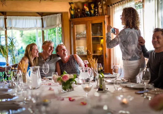 Five guests at meal, one taking photo of other three.