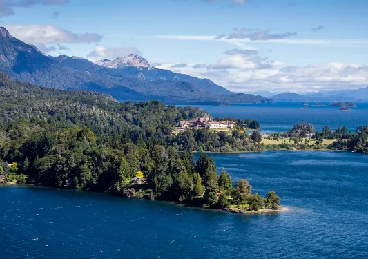 Wide shot of inlet, white building, snowy peak, larger lake in distance.