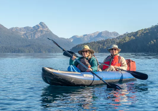 Two guests kayaking, sharp mountains in distance.