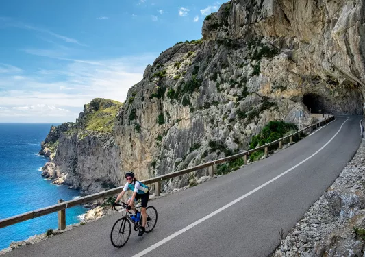 Guest cycling down coastal cliffside road, road coming from cave, ocean to  her right.