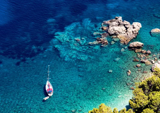 Bird's eye shot of rocky beach, small boat, blue water.