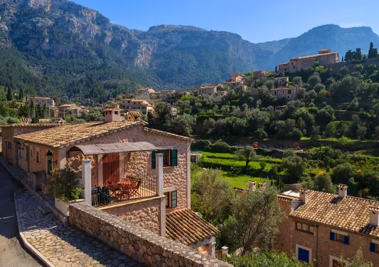 Shot of Italian mountain village, tan stone houses, trees, mountains all around.