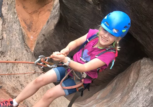 Young guest rock climbing on cliffside, smiling at camera.