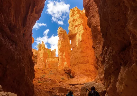 Guests hiking between orange hoodoos, blue sky above.