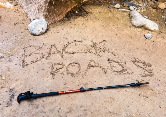 Shot of hiking pole on trail, "Backroads" etched into the mud above.