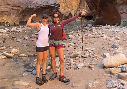 Female hikers in canyon narrows: arms out, guns out