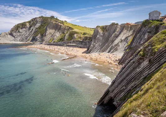 Shot of craggy cliffs, large, crowded beach in distance. 