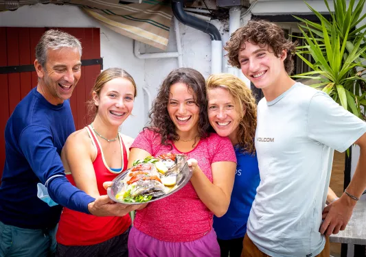 Group of guests holding plate of fish, showing it to camera.
