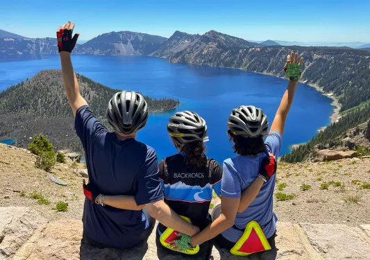 Three guests with their hands above their heads, celebrating on he rim of Crater Lake.