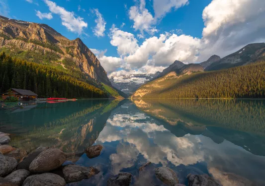 Wide shot of lake, wooden shack, mountain range, valley.