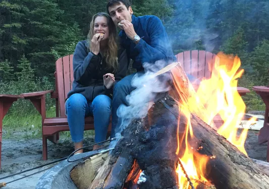 Two guests eating smores around a fire.