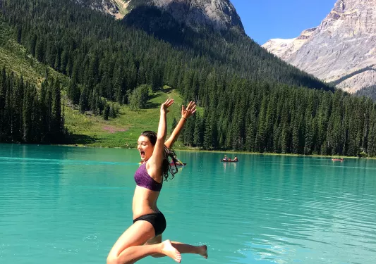 Guest jumping into light blue lake, mountain in background.