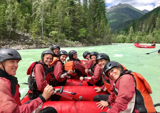 Group of guests in raft, white water in distance.