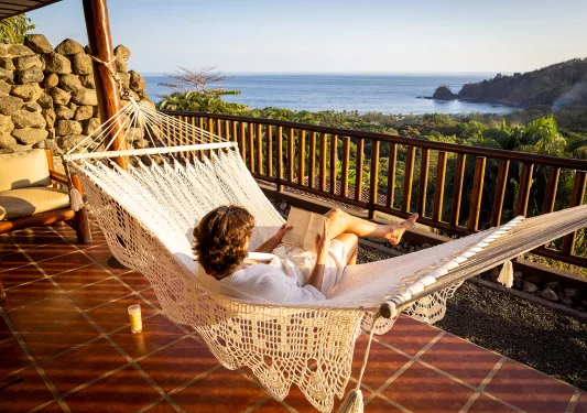 Guest on hotel balcony, hammock, overlooking forest, ocean.