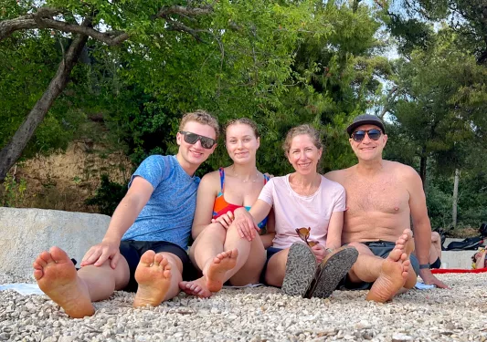 Group of guests on rocky beach, smiling at camera, trees behind.