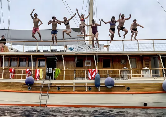 Group of guests jumping off large wood panel boat.