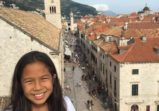 Young guest on balcony, smiling, overlooking crowded Dubrovnik street.