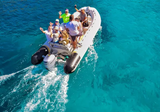 Group of guests on inflatable boat, waving to camera.