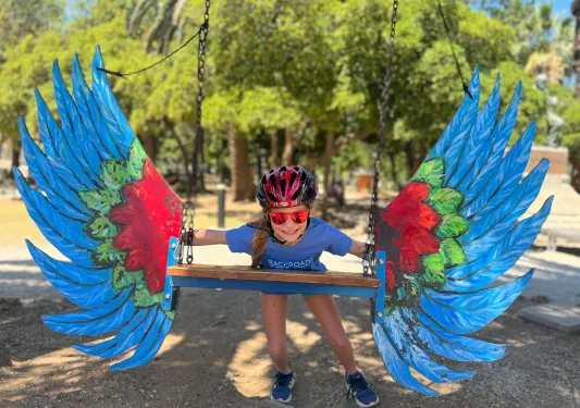 Young guest in bike gear on swing, colorful bird wings attached to it.