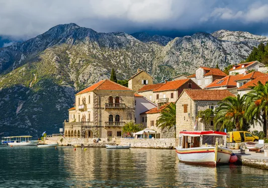 Shot of Croatian houses on coast, boats, mountain in distance.