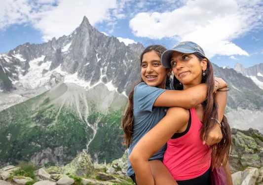 Two guests, one on the other's back, posing in front of large mountain vista.