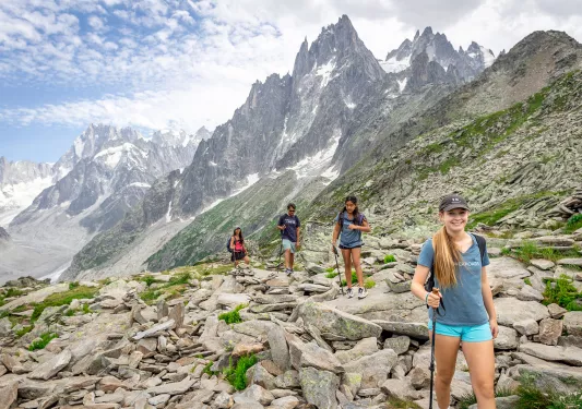 Four guests walking up craggy hillside, large, spiked mountains behind them.