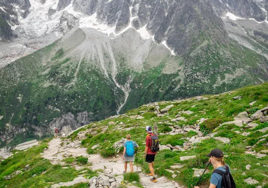 Three guests walking down mountainside, large, spiky peaks in distance. 