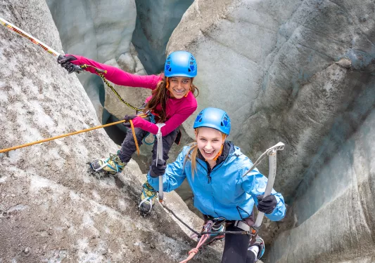 Two guests in climbing gear on a mountainside, both looking at camera.