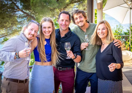 Five guests in nice clothes, wine glasses in hand smiling at camera.