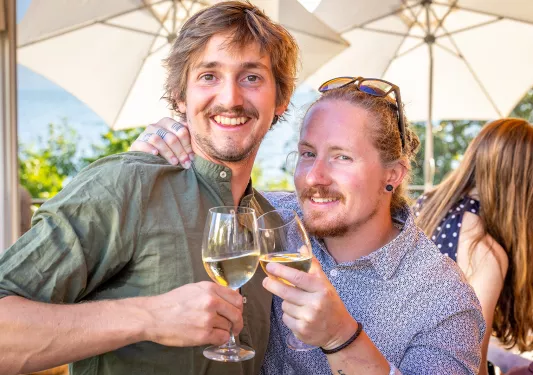 Two guests cheersing wine glasses, one with hand over other's shoulder.