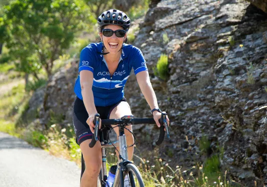 Guest cycling past rocks, smiling at camera.