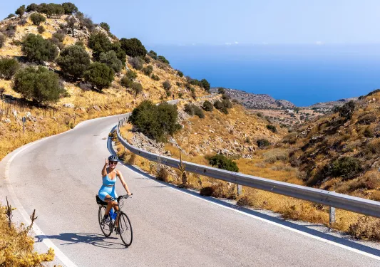 Guest cycling on golden coastal road, giving thumbs up, ocean behind.