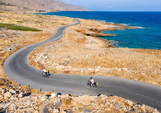 Two guests cycling along golden coastline, ocean to their right.