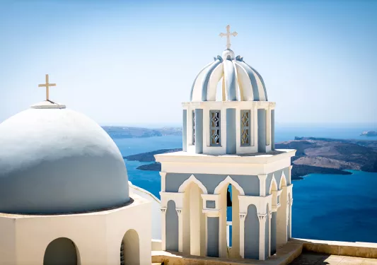 Close up of blue domes of Santorini, ocean behind them.