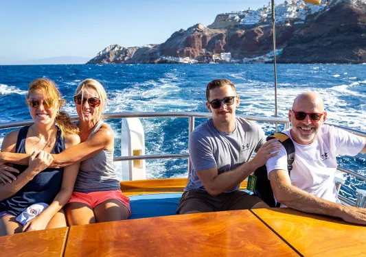 Four guests on rear of moving boat, rough water, island behind them.
