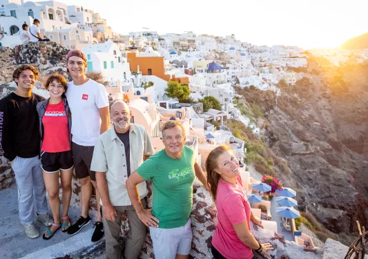 Group of guests among cliffside, whit houses, sunset behind them.