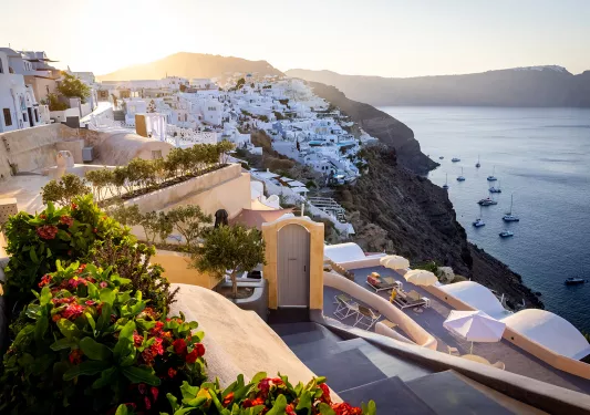 Wide shot of Santorini cliffside, white houses, ocean, sunset.
