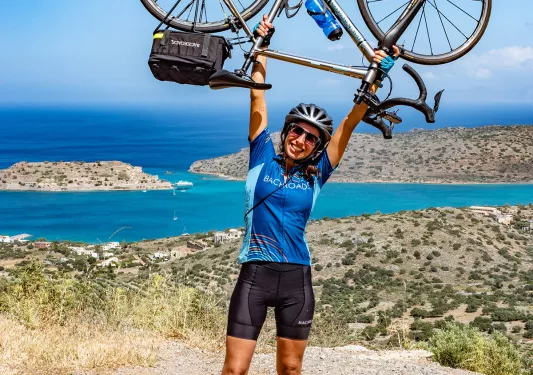 Guest on coastal road, holding bike above her head.