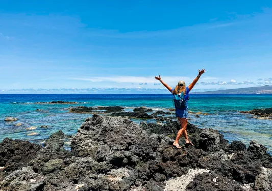 Woman walking towards the ocean with her arms in the air