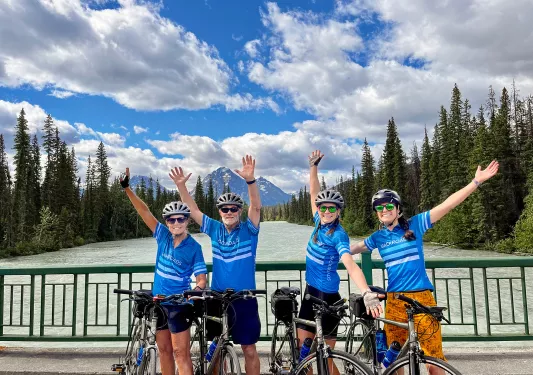 Four guests with arms outstretched, gesturing to trees, mountains.