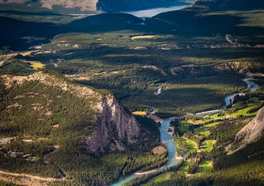 Bird's eye shot of huge mountain vista, trees, mountains rivers, clouds during sunset.
