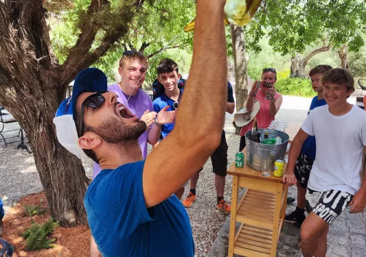 Group of guests amid forest, one pouring wine from ornate glass into mouth.
