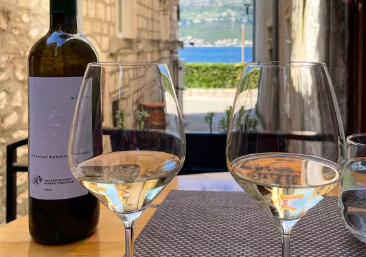 Close-up of red wine bottle, empty glasses, "BOKAR" sign behind.