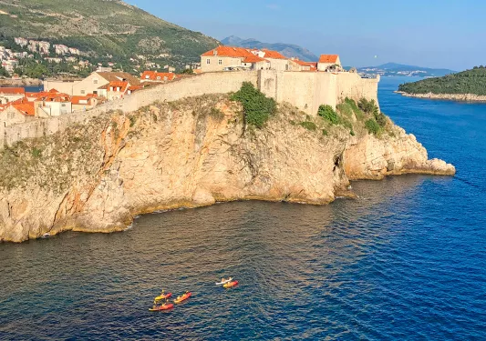 Wide shot of walled cliffside houses, guests kayaking below.