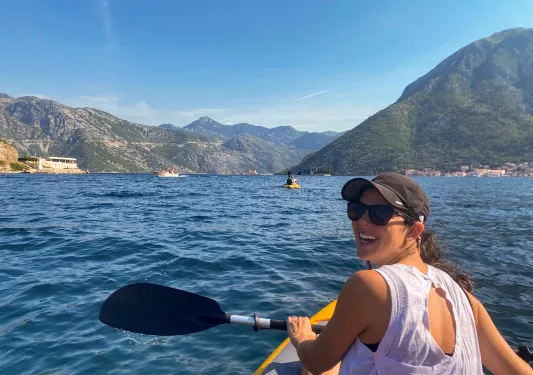Guest kayaking, looking at camera. Large mountains behind her.